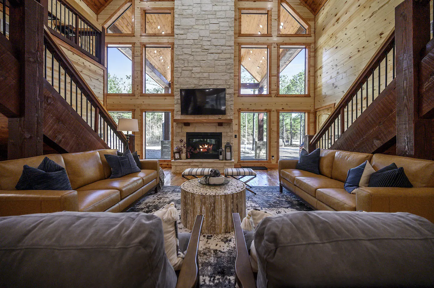 The family room boasts towering windows that allow natural sunlight to flood in, a substantial fireplace, a large-screen TV, and multiple seating areas.