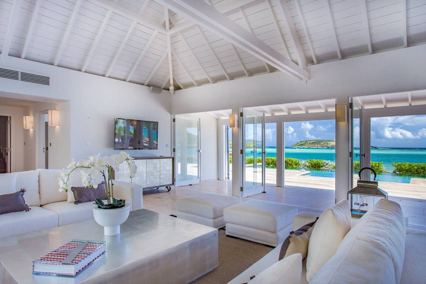 A spacious living area with floor-to-ceiling windows offering breathtaking views of the beach, furnished with comfortable seating and stylish decor.