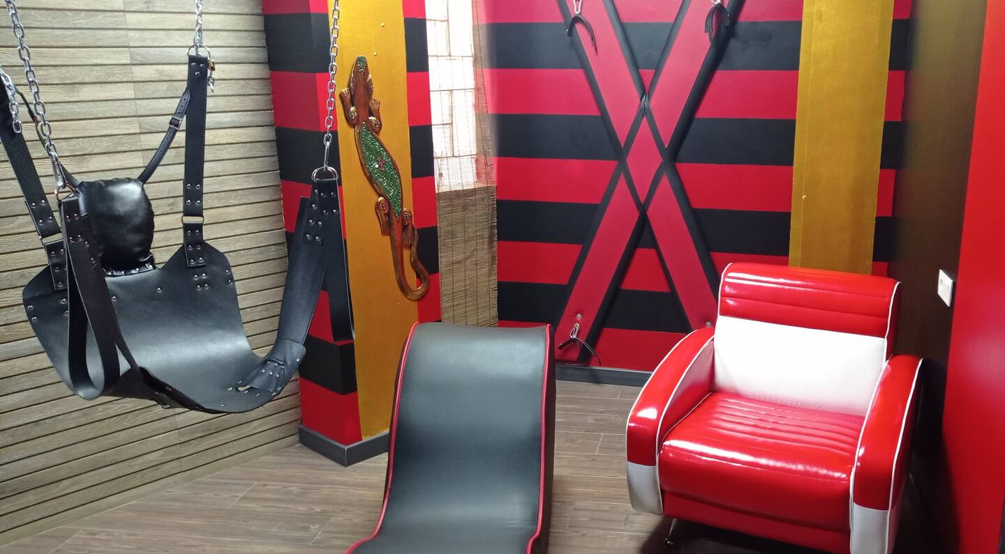 There's a playroom connected to the main bedroom, featuring a tantra chair, swing, cage, and a cross.